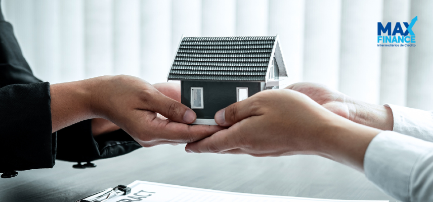 Duas pessoas a trocar uma casa miniatura com o logotipo Maxfinance 
